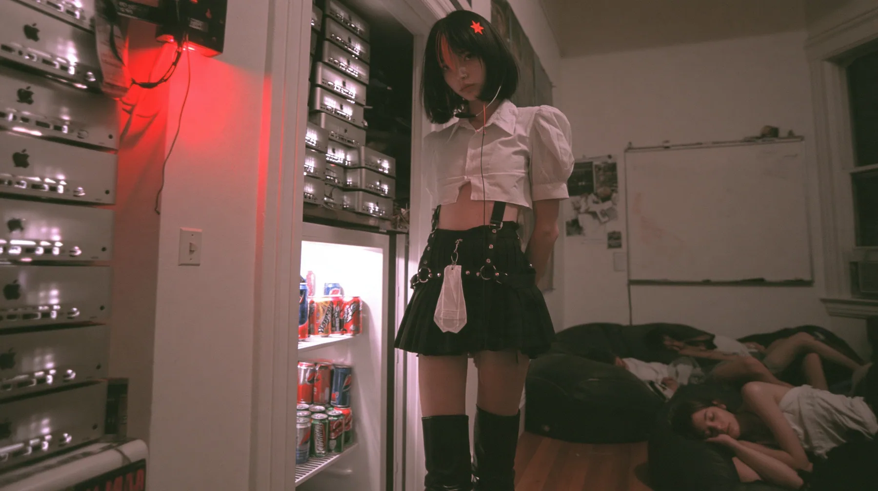 a San Francisco hacker house living room at 3am, stacks of Mac mini computers glowing on shelves and inside an open fridge beside energy drink cans, a whiteboard, people asleep on beanbags, a young Caucasian American…