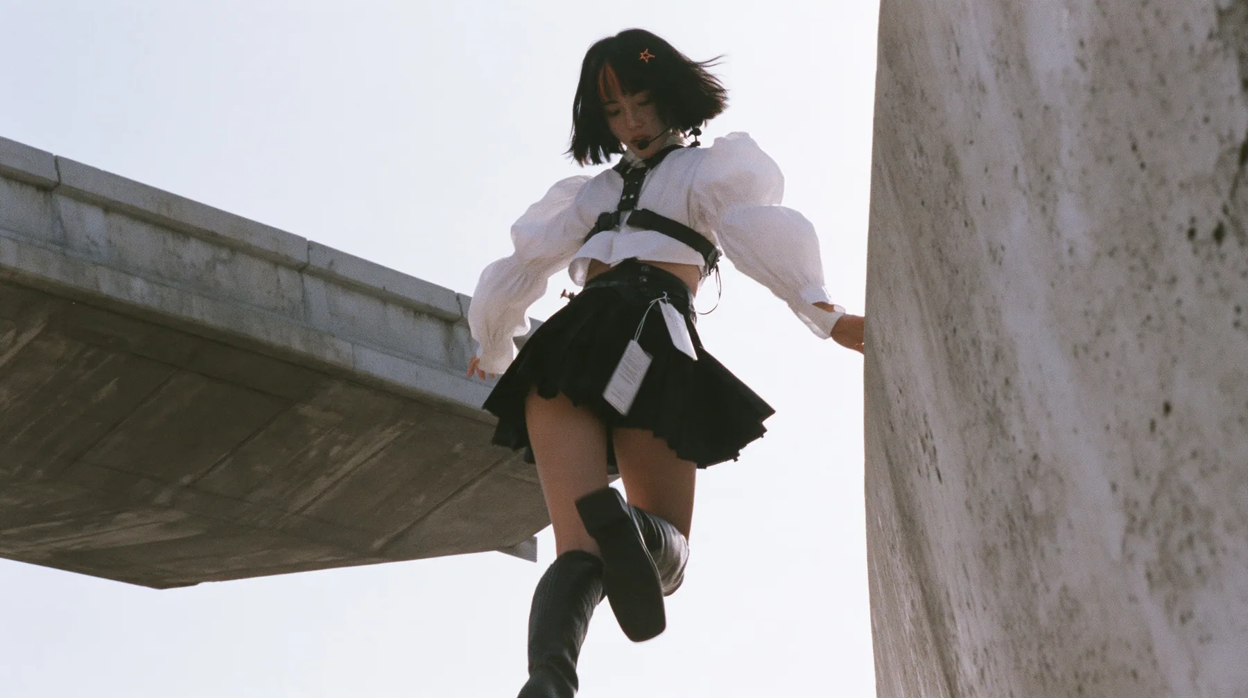 an elevated concrete freeway ramp that ends abruptly in the air against a pure white overexposed sky, a young Caucasian American woman with pale skin and light freckles, a glossy black blunt jaw-length bob with heavy…