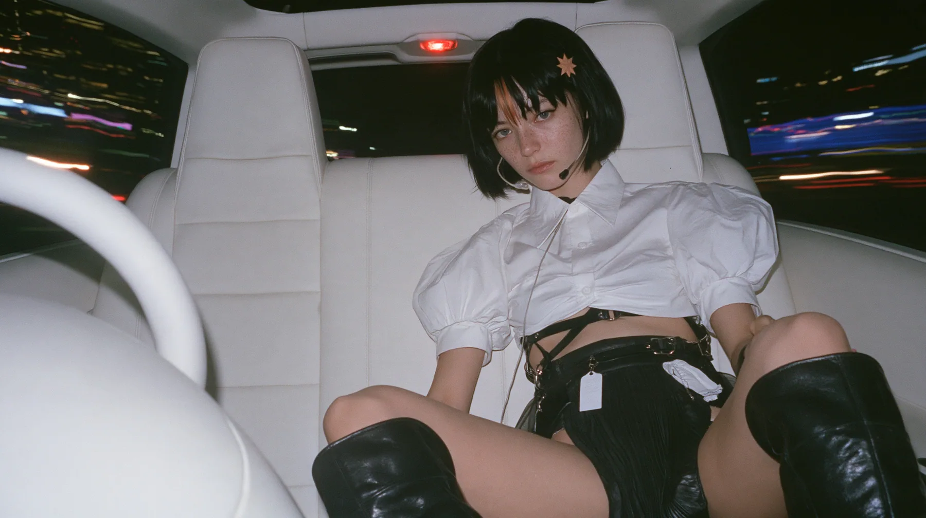 a young Caucasian American woman with pale skin and light freckles, a glossy black blunt jaw-length bob with heavy bangs and one clay-orange streak through the bangs, a small flat clay-orange eight-pointed star hair…