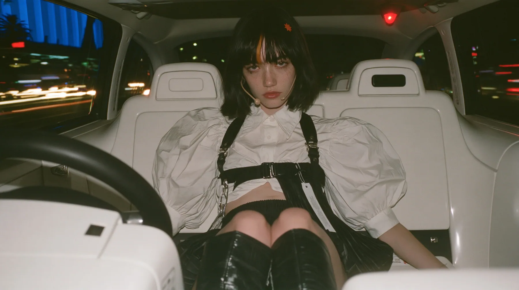 a young Caucasian American woman with pale skin and light freckles, a glossy black blunt jaw-length bob with heavy bangs and one clay-orange streak through the bangs, a small flat clay-orange eight-pointed star hair…