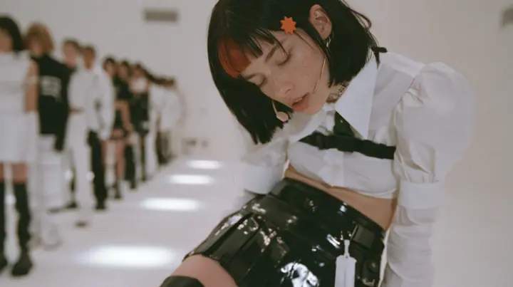 a young Caucasian American woman with pale skin and light freckles, a glossy black blunt jaw-length bob with heavy bangs and one clay-orange streak through the bangs, a small flat clay-orange eight-pointed star hair…