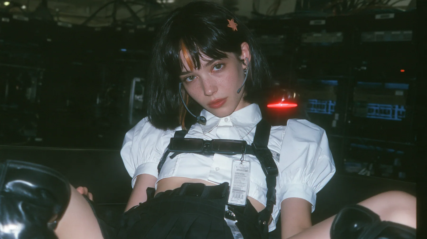 medium close-up of a young Caucasian American woman with pale skin and light freckles, a glossy black blunt jaw-length bob with heavy bangs and one clay-orange streak through the bangs, a small flat clay-orange…