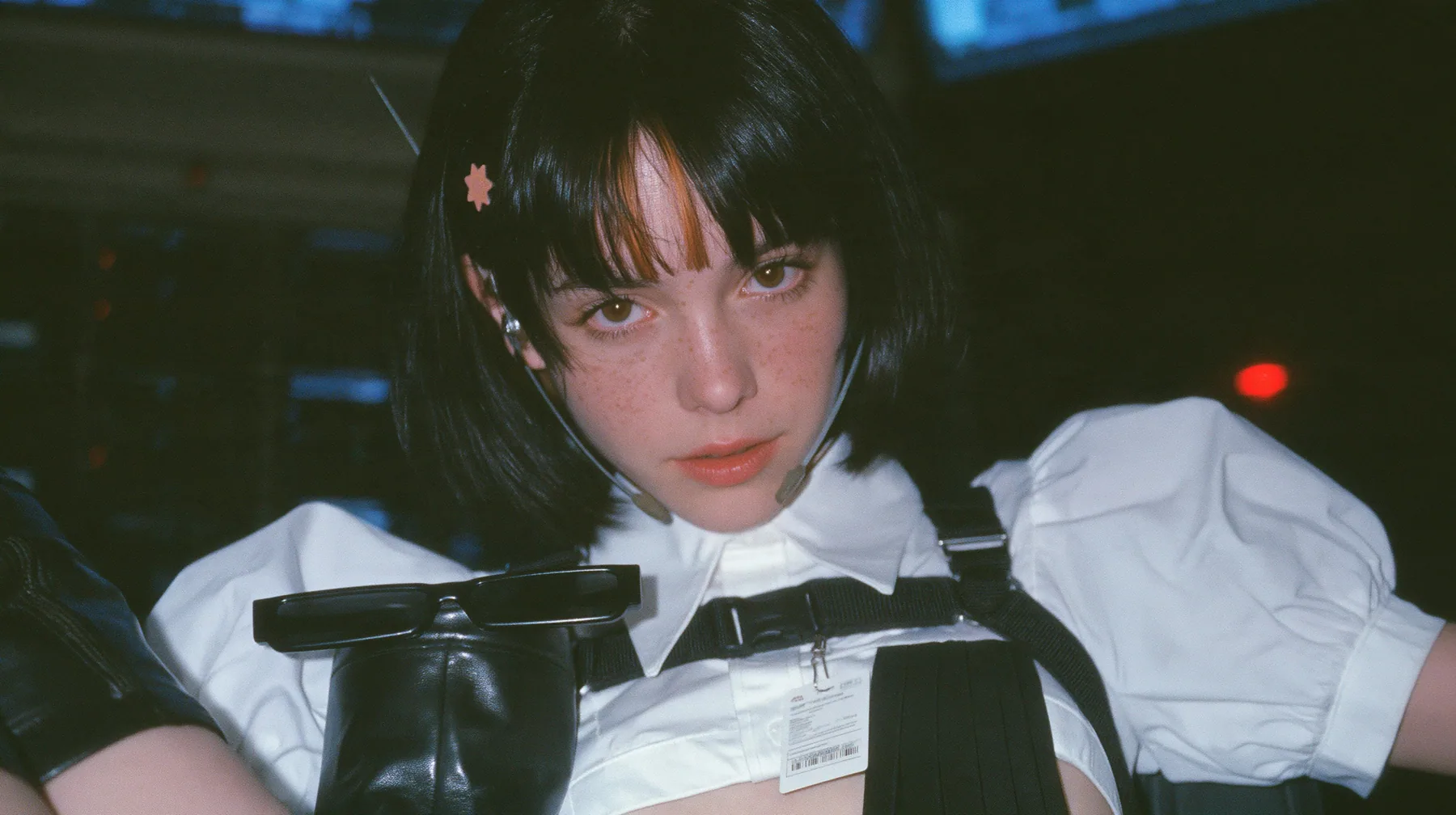 medium close-up of a young Caucasian American woman with pale skin and light freckles, a glossy black blunt jaw-length bob with heavy bangs and one clay-orange streak through the bangs, a small flat clay-orange…