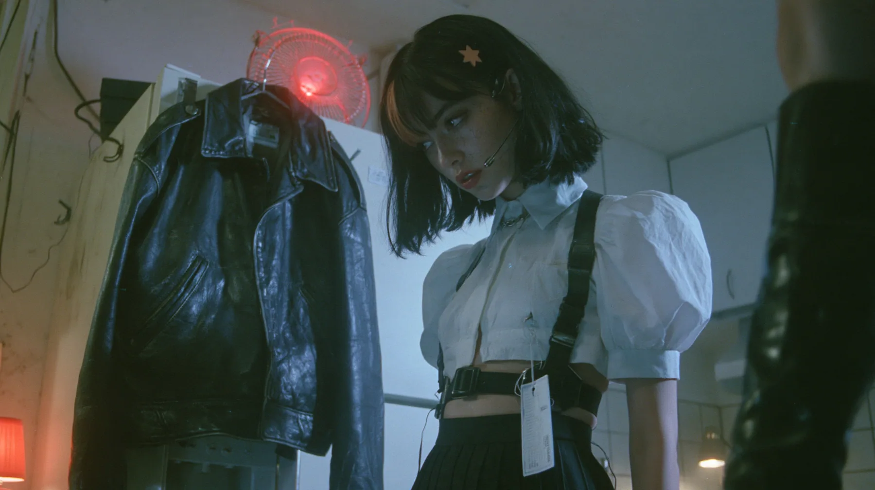 a black leather jacket hanging alone on a hook in a hacker house kitchen at night, a rotating red alarm beacon on top of a fridge, a young Caucasian American woman with pale skin and light freckles, a glossy black…