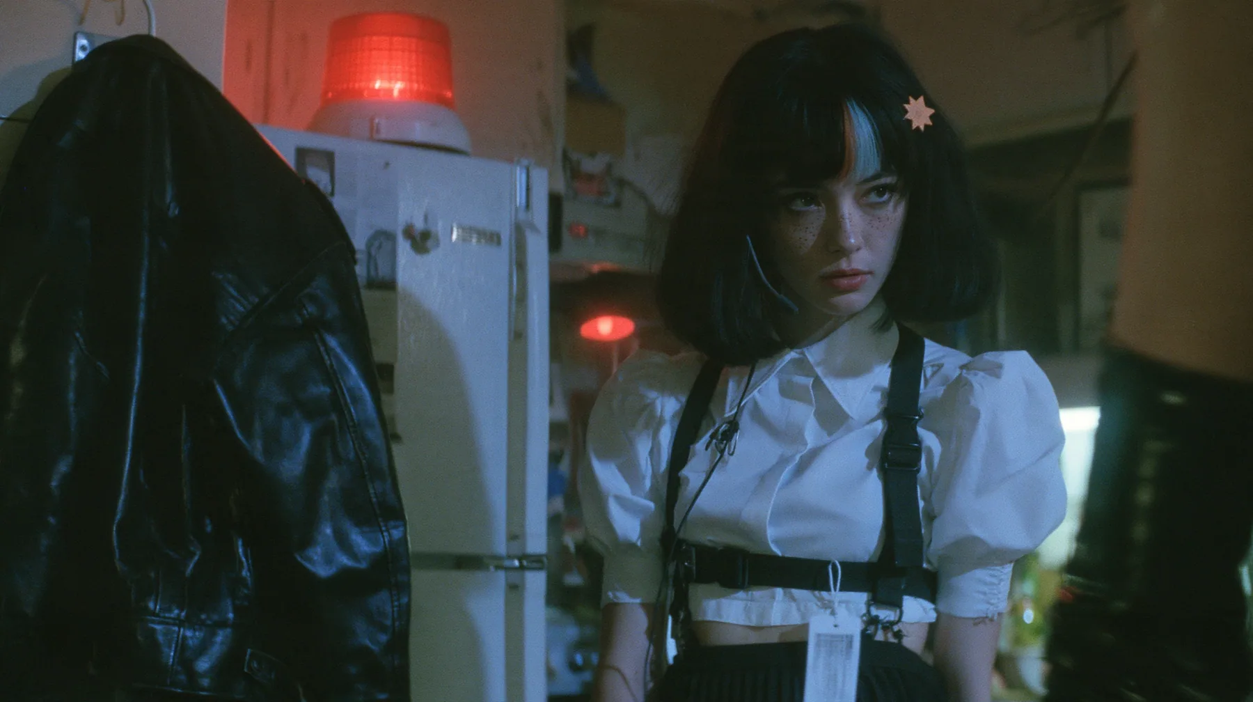 a black leather jacket hanging alone on a hook in a hacker house kitchen at night, a rotating red alarm beacon on top of a fridge, a young Caucasian American woman with pale skin and light freckles, a glossy black…