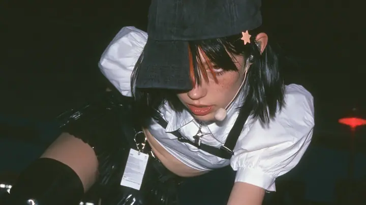 close-up of the plain front panel of a washed black baseball cap worn by a young Caucasian American woman with pale skin and light freckles, a glossy black blunt jaw-length bob with heavy bangs and one clay-orange…