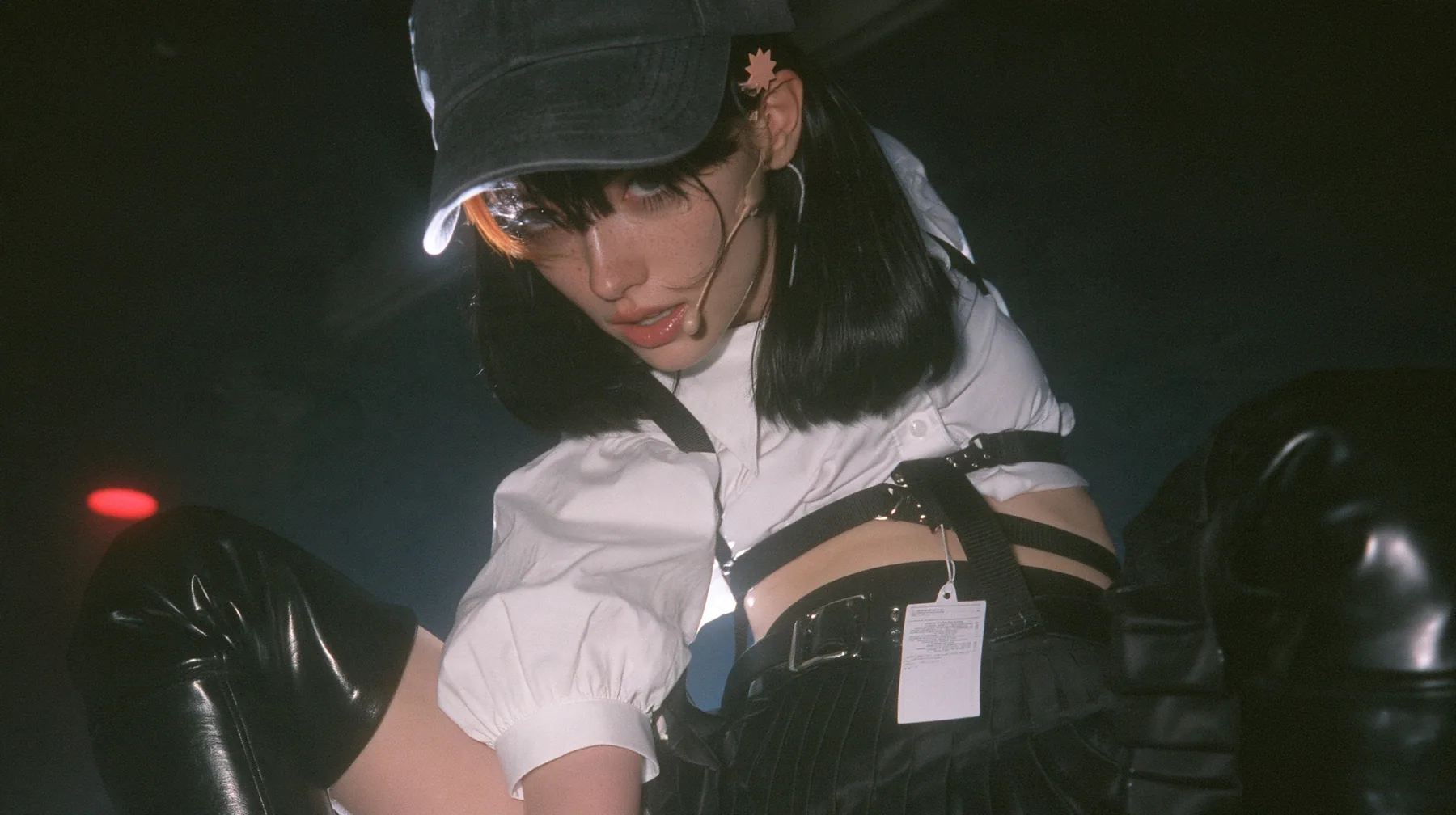 close-up of the plain front panel of a washed black baseball cap worn by a young Caucasian American woman with pale skin and light freckles, a glossy black blunt jaw-length bob with heavy bangs and one clay-orange…
