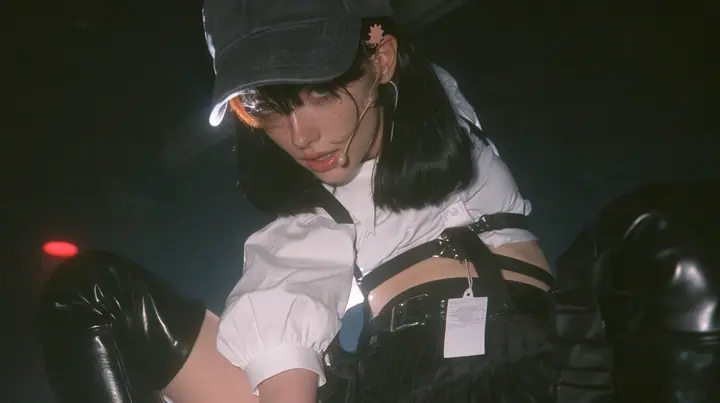 close-up of the plain front panel of a washed black baseball cap worn by a young Caucasian American woman with pale skin and light freckles, a glossy black blunt jaw-length bob with heavy bangs and one clay-orange…