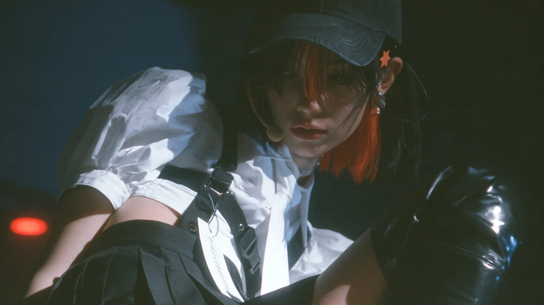 close-up of the plain front panel of a washed black baseball cap worn by a young Caucasian American woman with pale skin and light freckles, a glossy black blunt jaw-length bob with heavy bangs and one clay-orange…