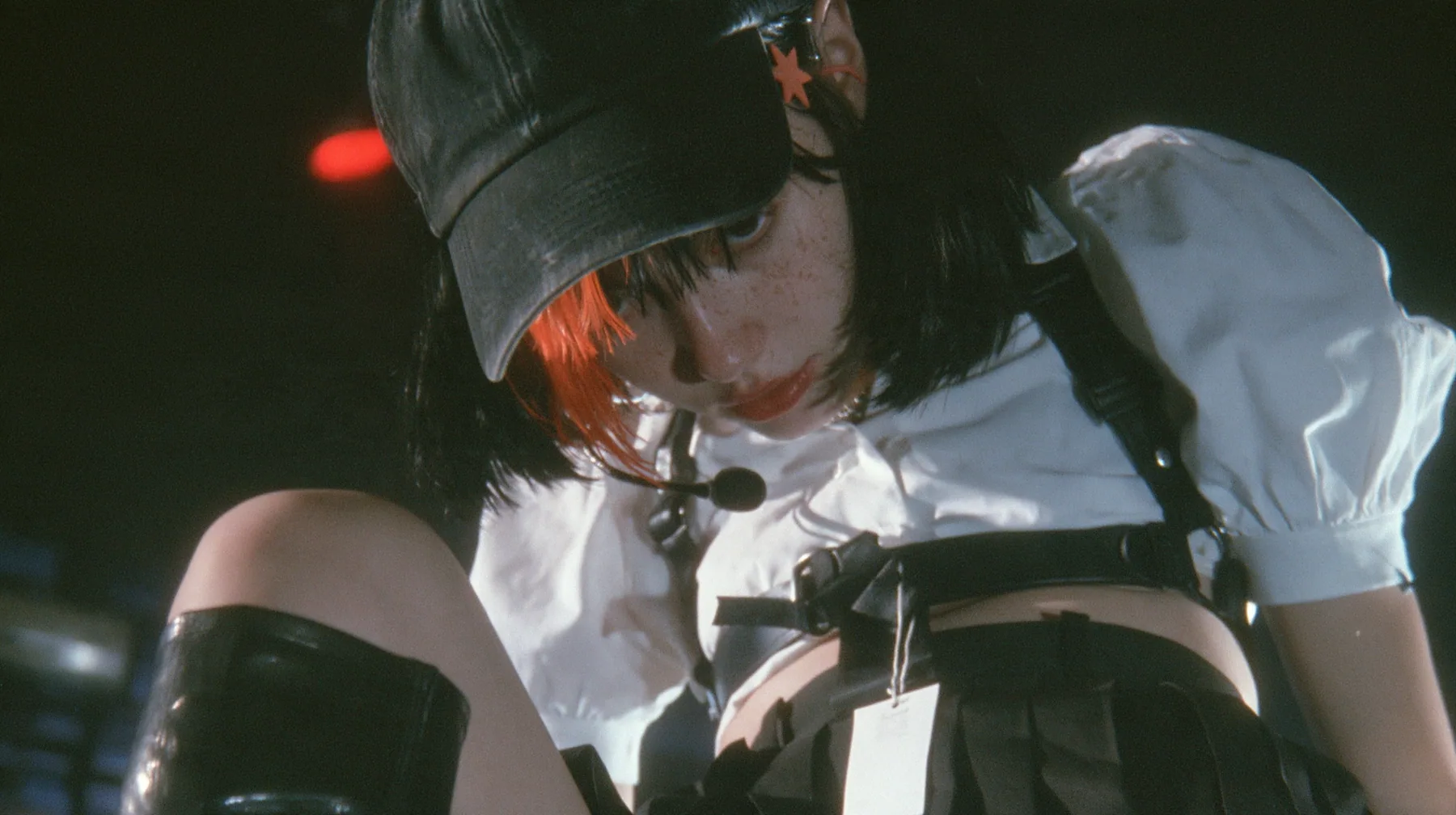 close-up of the plain front panel of a washed black baseball cap worn by a young Caucasian American woman with pale skin and light freckles, a glossy black blunt jaw-length bob with heavy bangs and one clay-orange…