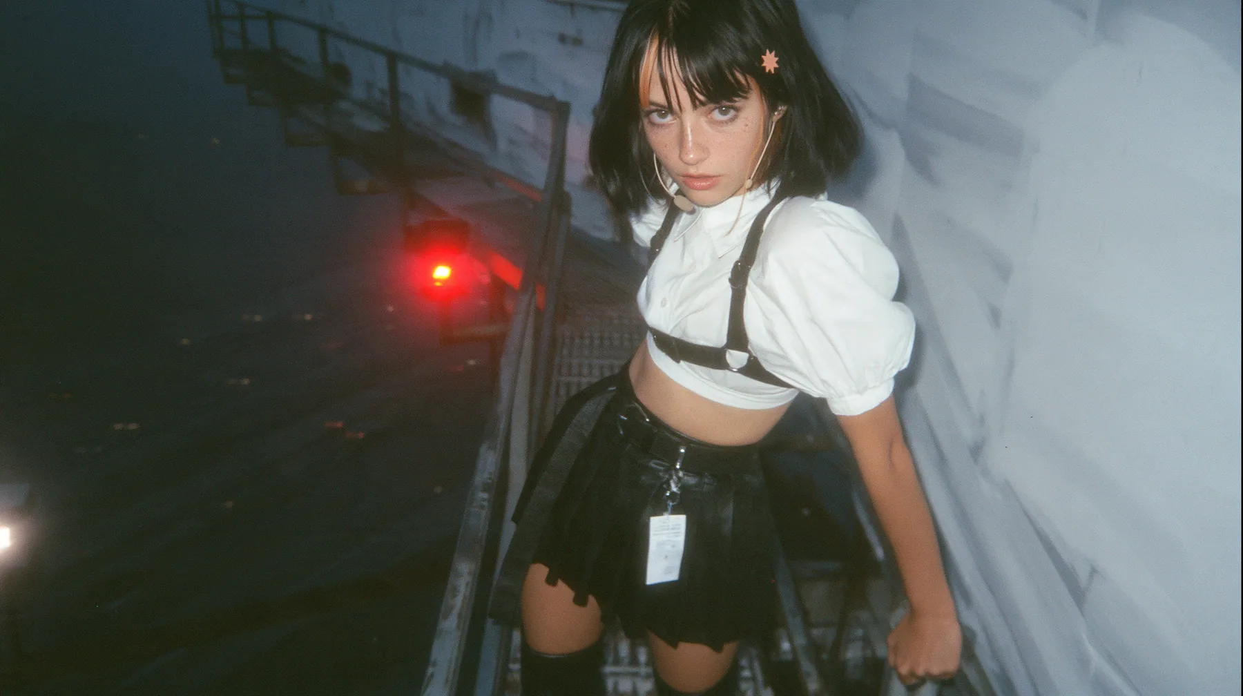 a young Caucasian American woman with pale skin and light freckles, a glossy black blunt jaw-length bob with heavy bangs and one clay-orange streak through the bangs, a small flat clay-orange eight-pointed star hair…