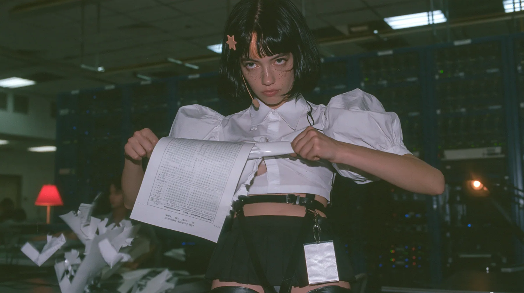 a young Caucasian American woman with pale skin and light freckles, a glossy black blunt jaw-length bob with heavy bangs and one clay-orange streak through the bangs, a small flat clay-orange eight-pointed star hair…