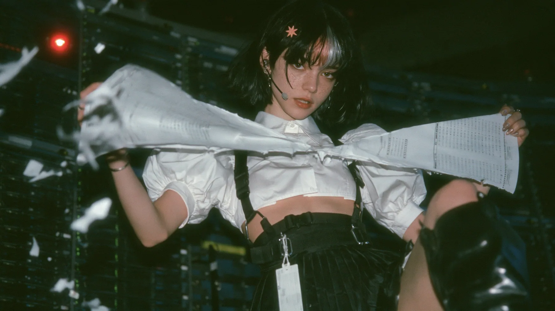 a young Caucasian American woman with pale skin and light freckles, a glossy black blunt jaw-length bob with heavy bangs and one clay-orange streak through the bangs, a small flat clay-orange eight-pointed star hair…