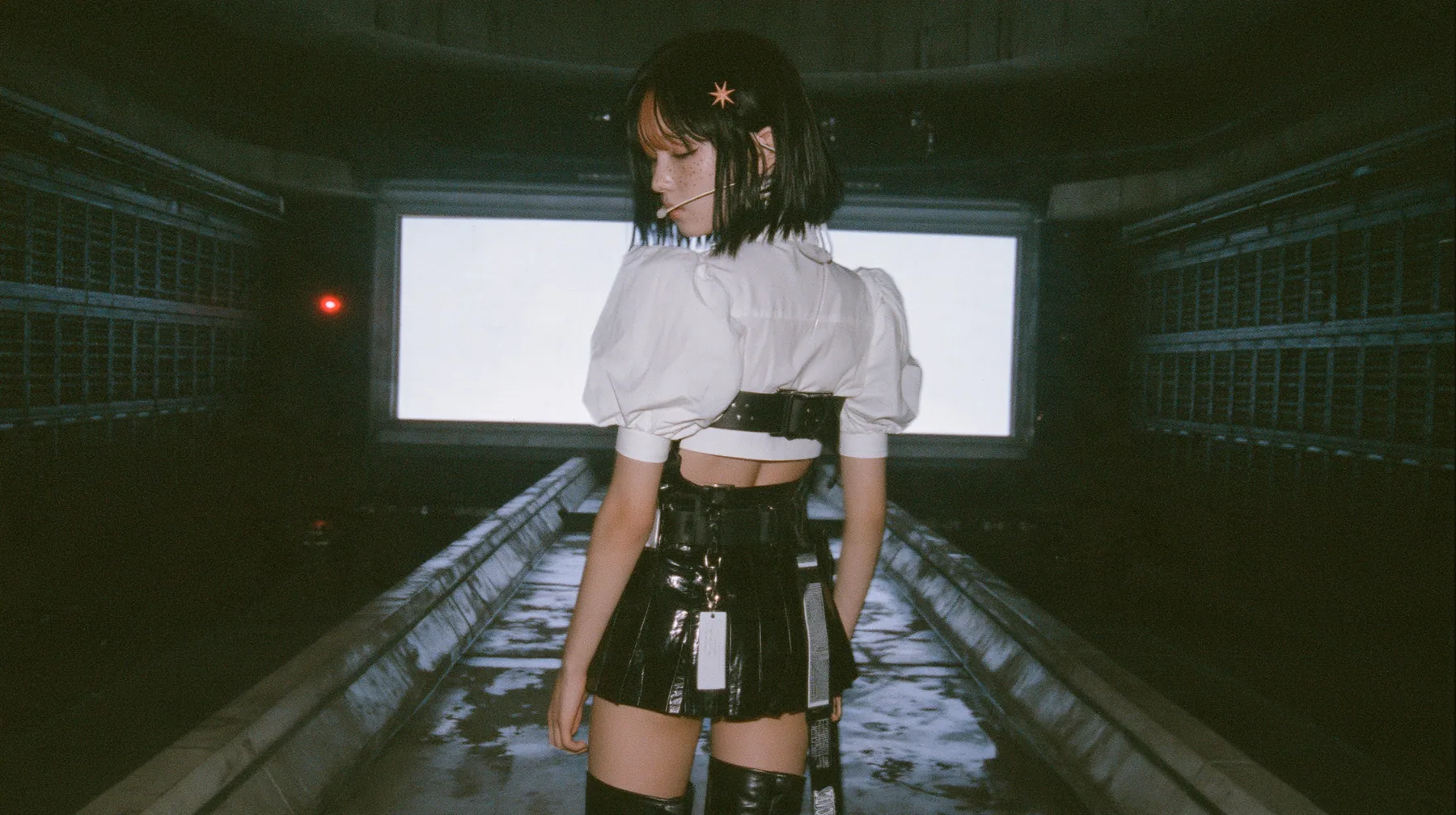 a young Caucasian American woman with pale skin and light freckles, a glossy black blunt jaw-length bob with heavy bangs and one clay-orange streak through the bangs, a small flat clay-orange eight-pointed star hair…