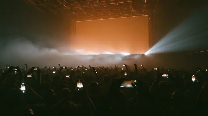 a dark crowd of front-row spectators raising glowing phones above their heads in a data hall, backlit fog, warm light from a giant board behind, blue-black night turning to first light, clay-orange #D97757 light as…
