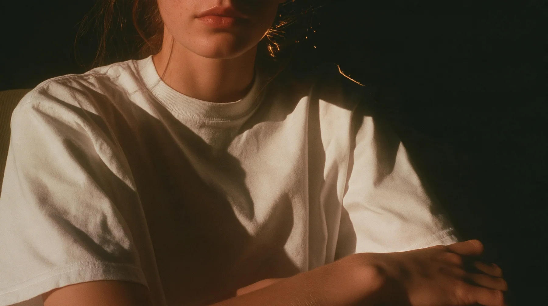 a front-row spectator in a plain white t-shirt seated in the dark, arms folded, face cropped at the chin, warm light, blue-black night turning to first light, clay-orange #D97757 light as the only colour, fine grain,…