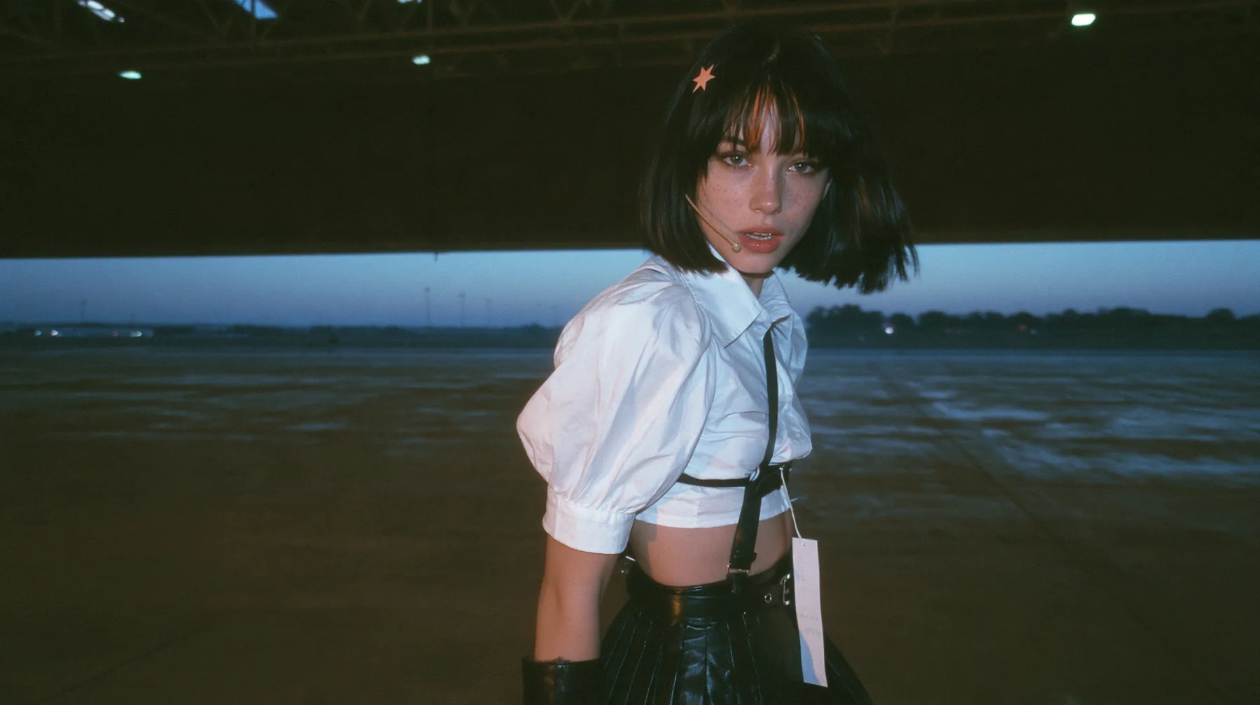 the far wall of a vast dark hall lifting like a giant garage door, a band of pale grey pre-dawn light spreading across the wet floor, a young Caucasian American woman with pale skin and light freckles, a glossy black…