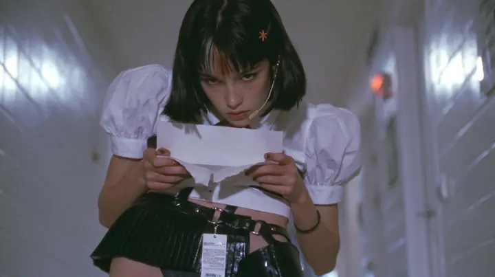 a young Caucasian American woman with pale skin and light freckles, a glossy black blunt jaw-length bob with heavy bangs and one clay-orange streak through the bangs, a small flat clay-orange eight-pointed star hair…