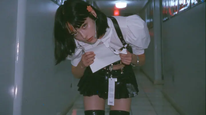 a young Caucasian American woman with pale skin and light freckles, a glossy black blunt jaw-length bob with heavy bangs and one clay-orange streak through the bangs, a small flat clay-orange eight-pointed star hair…