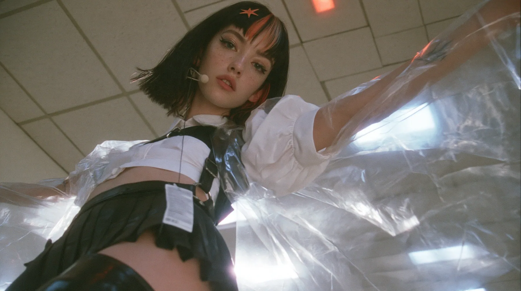 a young Caucasian American woman with pale skin and light freckles, a glossy black blunt jaw-length bob with heavy bangs and one clay-orange streak through the bangs, a small flat clay-orange eight-pointed star hair…