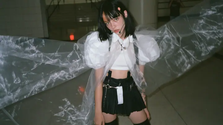 a young Caucasian American woman with pale skin and light freckles, a glossy black blunt jaw-length bob with heavy bangs and one clay-orange streak through the bangs, a small flat clay-orange eight-pointed star hair…