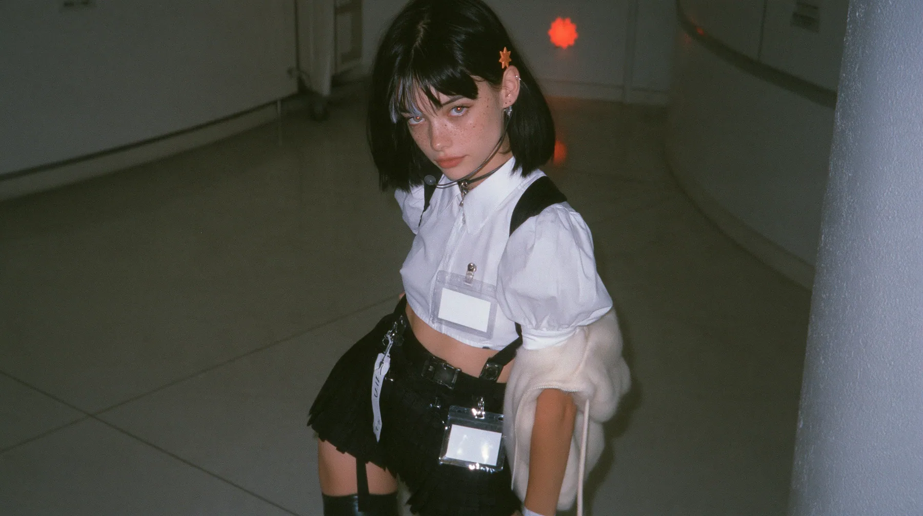 a young Caucasian American woman with pale skin and light freckles, a glossy black blunt jaw-length bob with heavy bangs and one clay-orange streak through the bangs, a small flat clay-orange eight-pointed star hair…