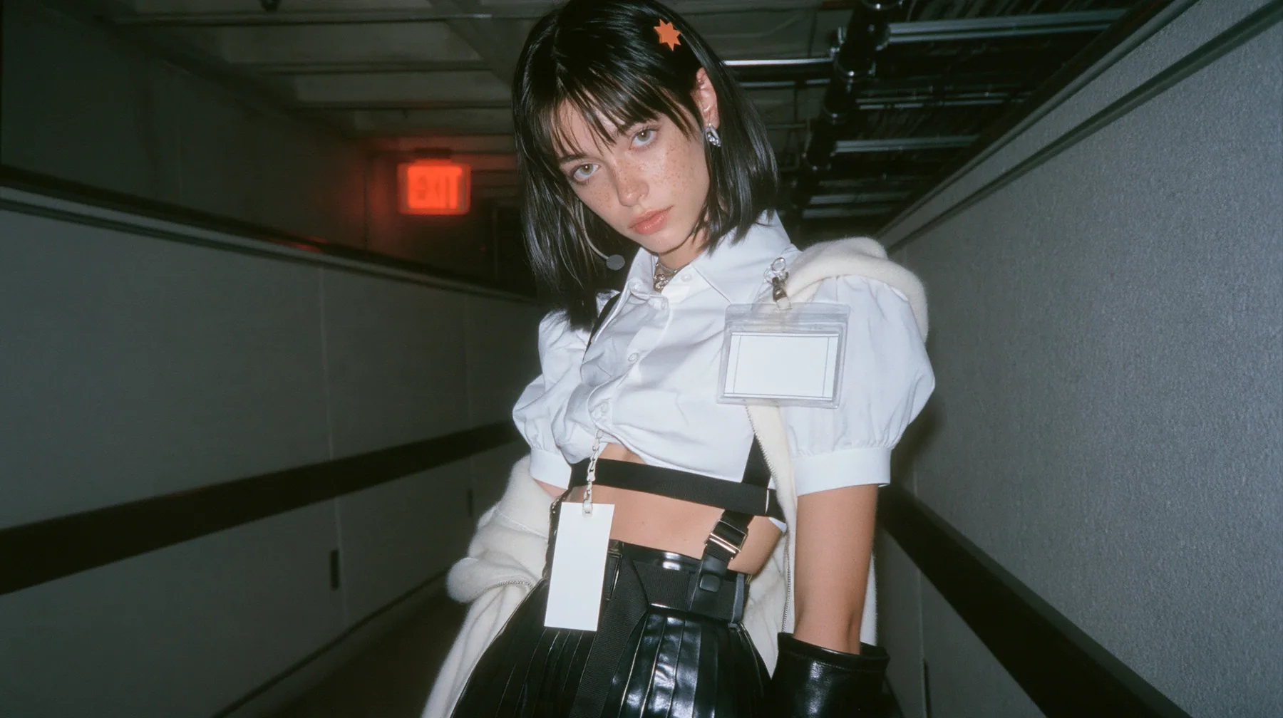a young Caucasian American woman with pale skin and light freckles, a glossy black blunt jaw-length bob with heavy bangs and one clay-orange streak through the bangs, a small flat clay-orange eight-pointed star hair…
