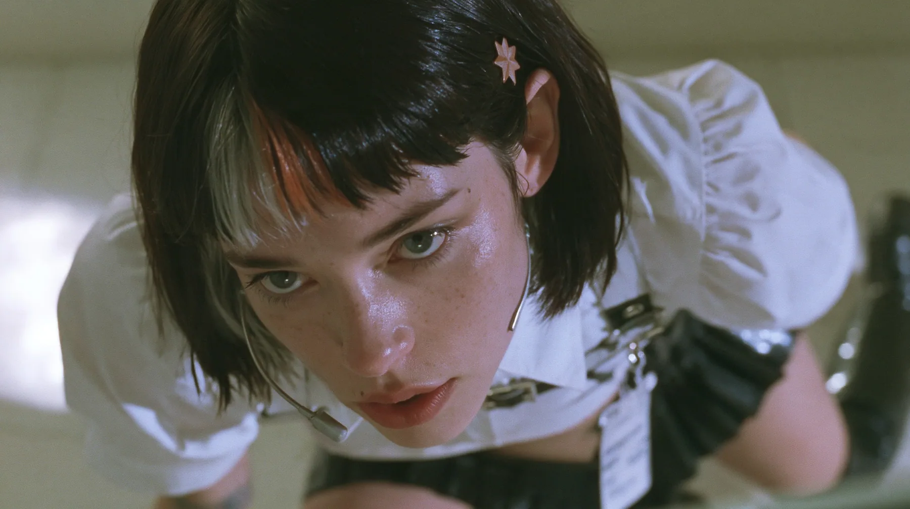 close-up of a young Caucasian American woman with pale skin and light freckles, a glossy black blunt jaw-length bob with heavy bangs and one clay-orange streak through the bangs, a small flat clay-orange…