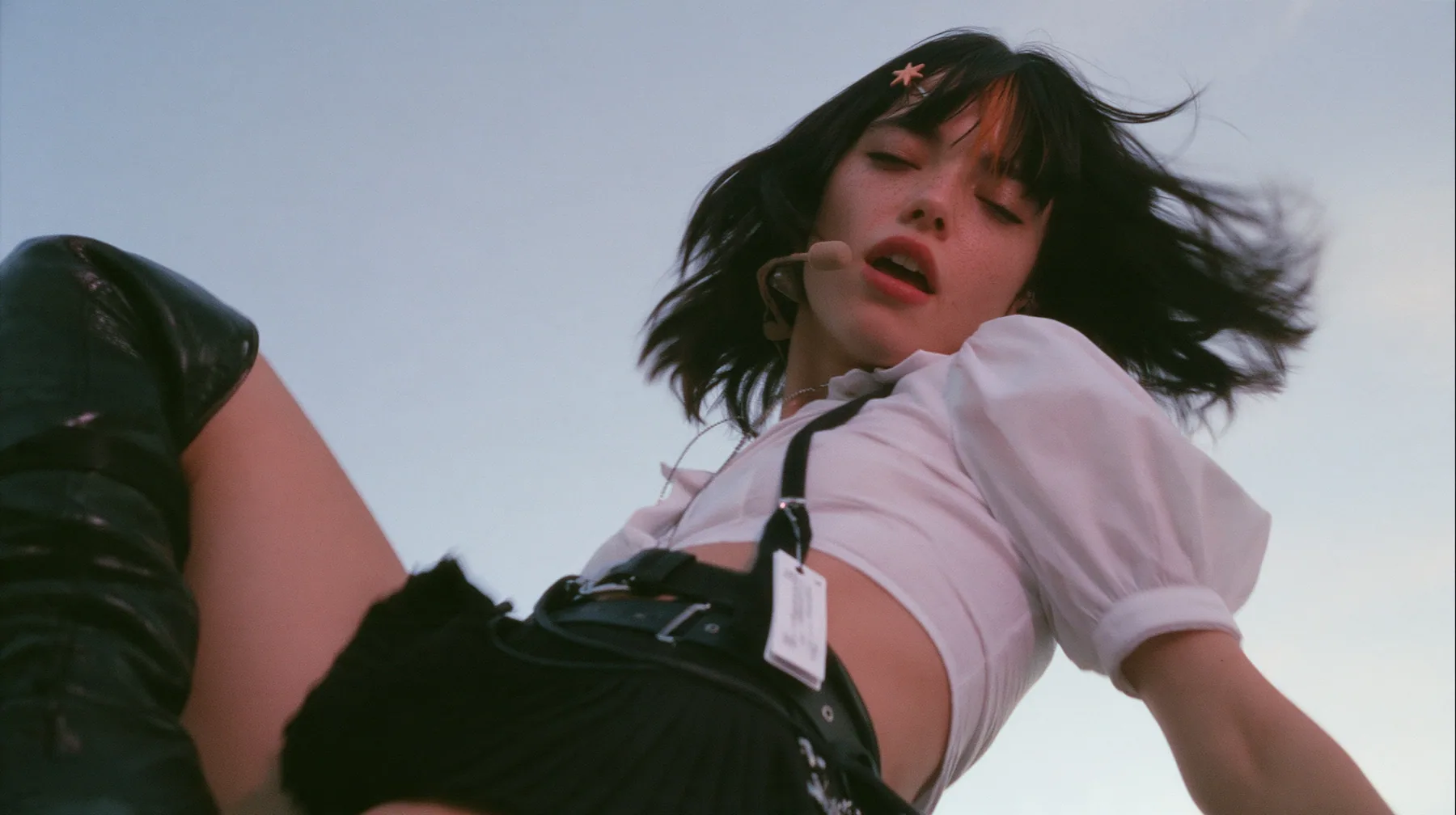close-up of a young Caucasian American woman with pale skin and light freckles, a glossy black blunt jaw-length bob with heavy bangs and one clay-orange streak through the bangs, a small flat clay-orange…