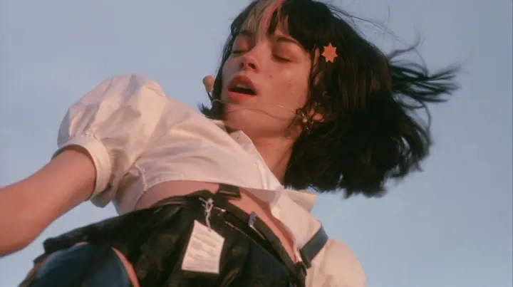 close-up of a young Caucasian American woman with pale skin and light freckles, a glossy black blunt jaw-length bob with heavy bangs and one clay-orange streak through the bangs, a small flat clay-orange…