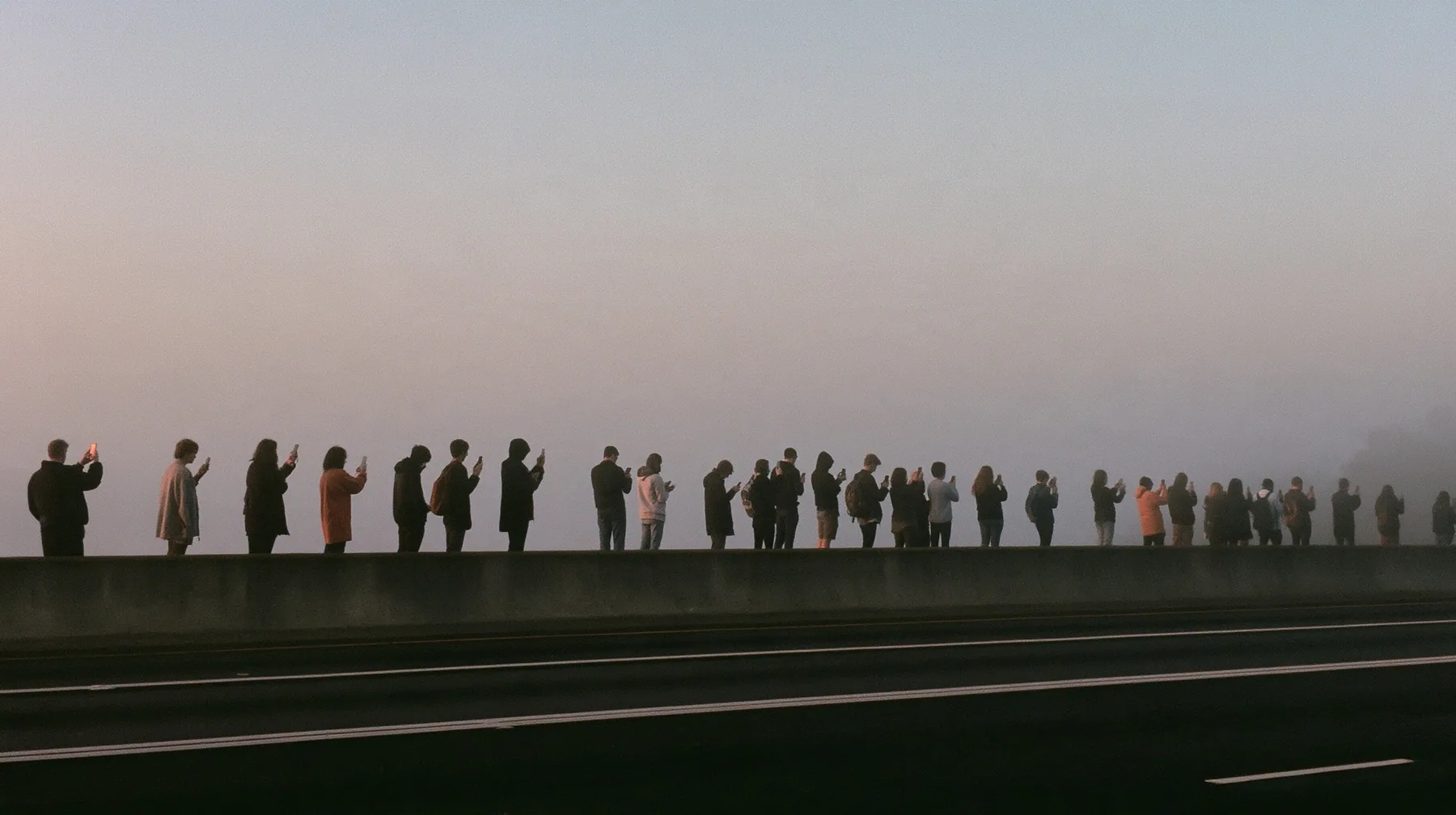 a line of spectators along a freeway barrier at dawn holding phones up, fog below, pale dawn grey-white, soft even light, a single clay-orange #D97757 accent, fine grain, calm, no text, no letters, no logos