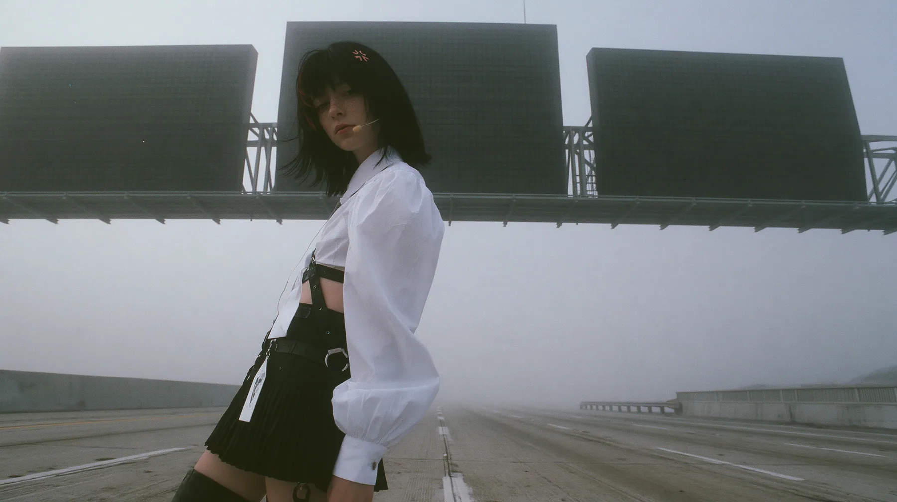 three enormous split-flap signs on steel gantries spanning an empty freeway in white fog, blank black flaps, a young Caucasian American woman with pale skin and light freckles, a glossy black blunt jaw-length bob…