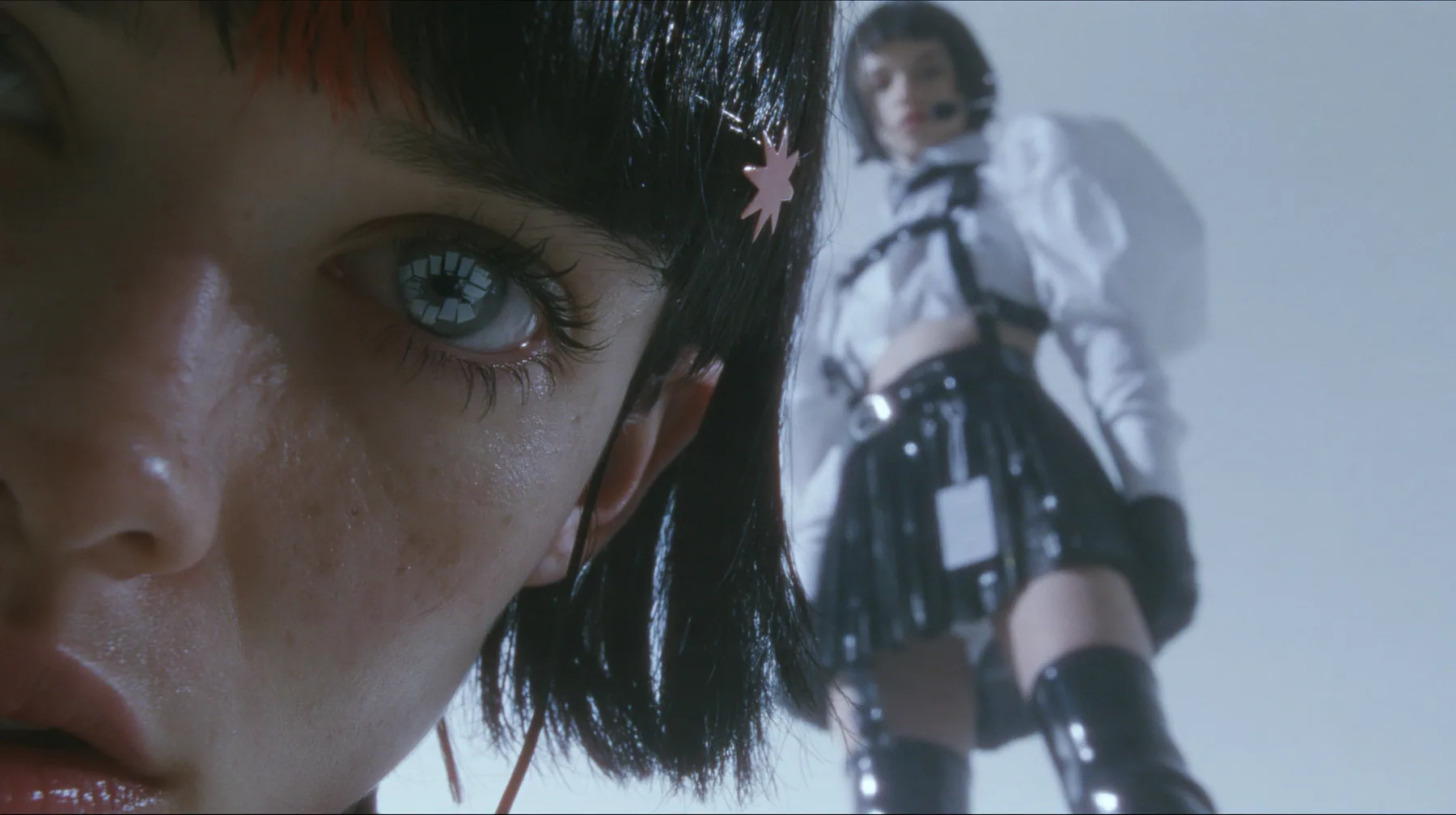 extreme close-up of an eye of a young Caucasian American woman with pale skin and light freckles, a glossy black blunt jaw-length bob with heavy bangs and one clay-orange streak through the bangs, a small flat…