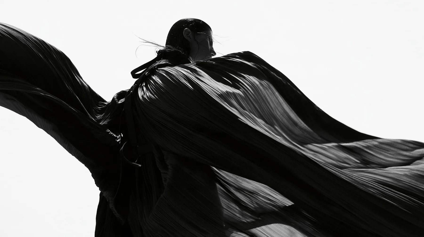 a huge black pleated fabric whipping in wind against a white void, harness straps flying, high-key white void, pure white paper light, hard clean black shadows, monochrome, no text, no letters, no logos