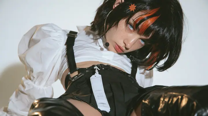 the hips of a young Caucasian American woman with pale skin and light freckles, a glossy black blunt jaw-length bob with heavy bangs and one clay-orange streak through the bangs, a small flat clay-orange…