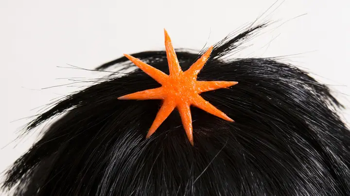 extreme close-up of an eight-pointed clay-orange spark hair clip in black hair against white, high-key white paper, one clay-orange #D97757 accent as the only colour, soft shadowless light, no text, no letters, no logos