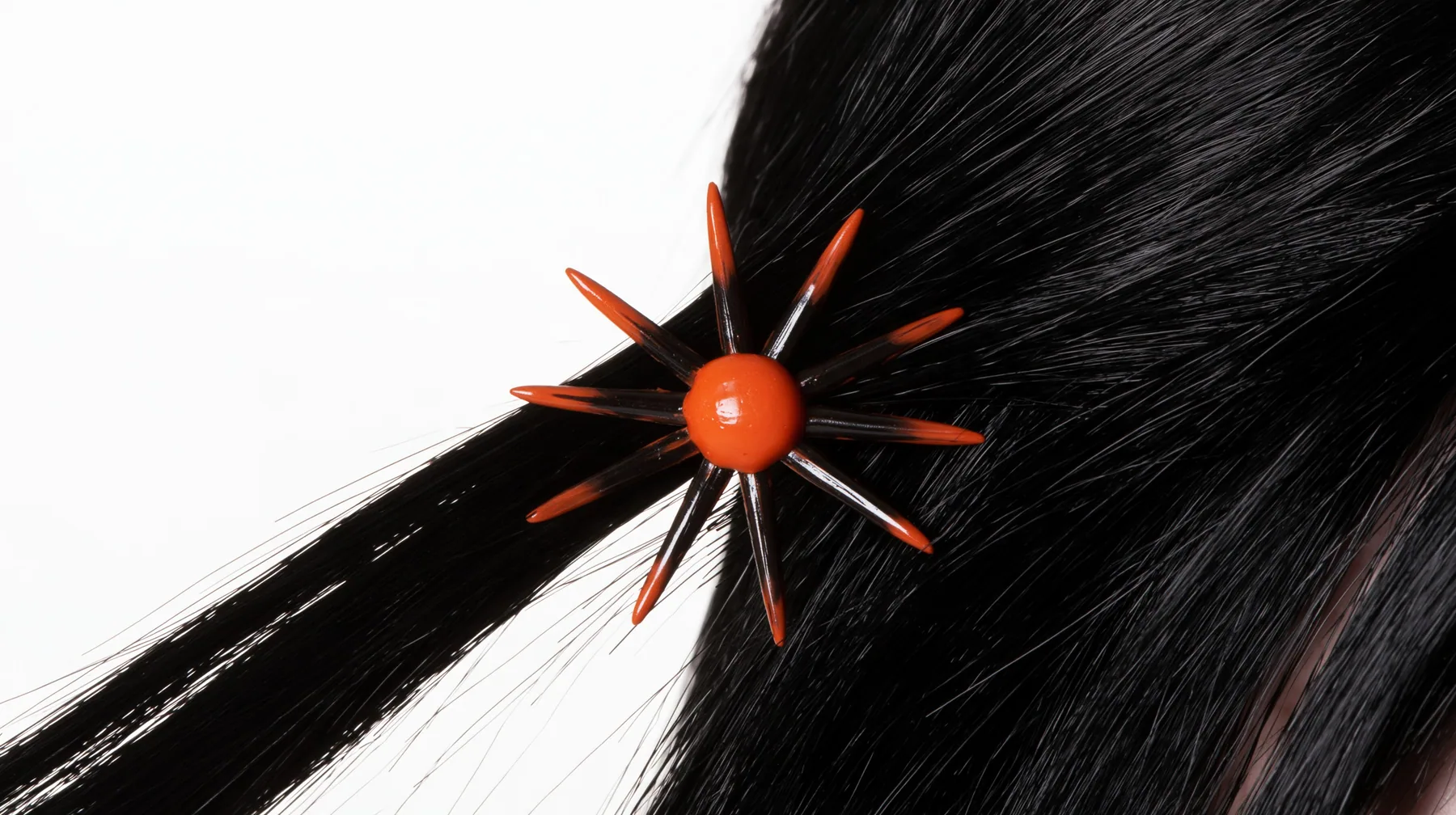 extreme close-up of an eight-pointed clay-orange spark hair clip in black hair against white, high-key white paper, one clay-orange #D97757 accent as the only colour, soft shadowless light, no text, no letters, no logos