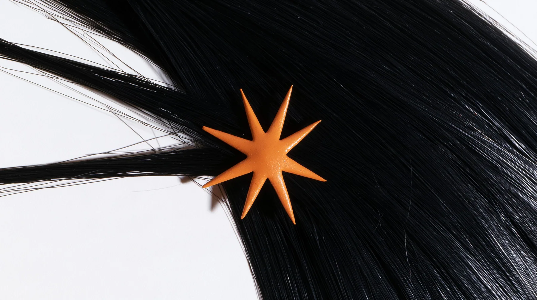 extreme close-up of an eight-pointed clay-orange spark hair clip in black hair against white, high-key white paper, one clay-orange #D97757 accent as the only colour, soft shadowless light, no text, no letters, no logos