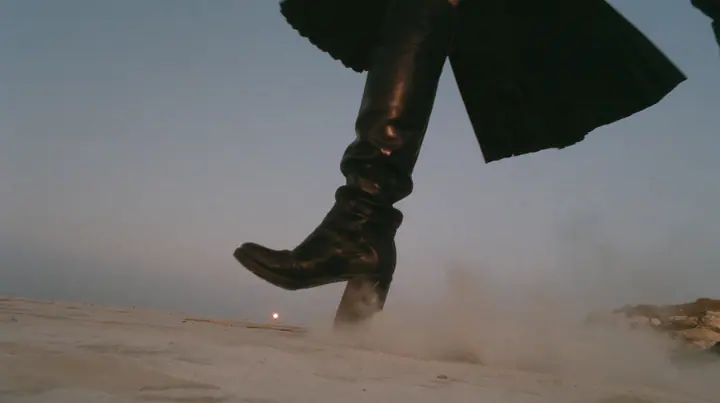 low close-up of a black knee boot stamping down on pale concrete, a puff of dust, a pleated black skirt hem at the top of the frame, no face, pale dawn grey-white, soft even light, a sea of fog below, one small…