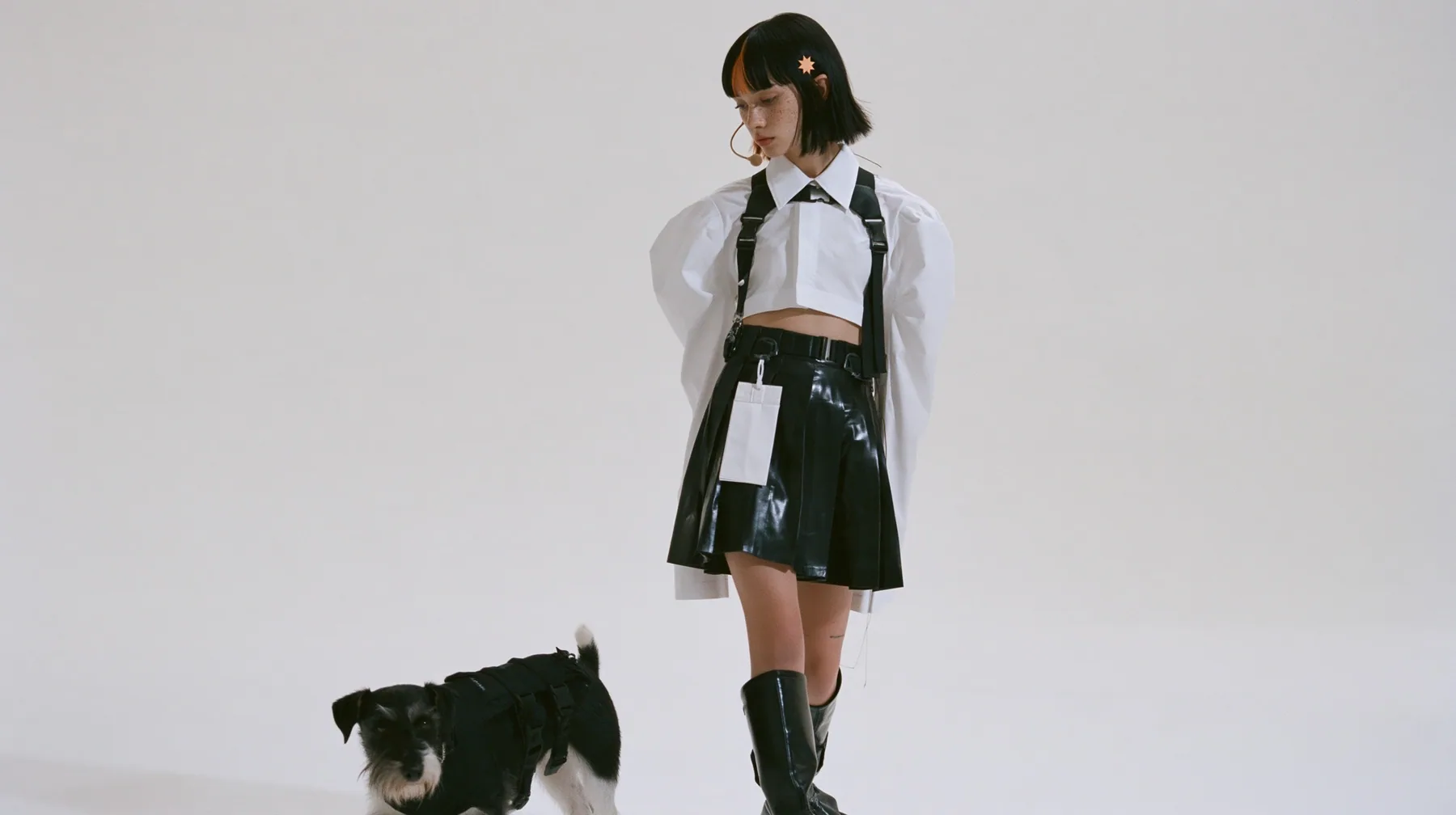 full-length shot of a young Caucasian American woman with pale skin and light freckles, a glossy black blunt jaw-length bob with heavy bangs and one clay-orange streak through the bangs, a small flat clay-orange…