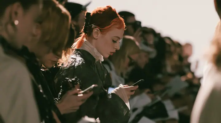 wide shot of a fashion show front row in high-key white light, the guests standing up and putting their phones away, faces cropped at the top of the frame, high-key white paper, soft shadowless light, monochrome…