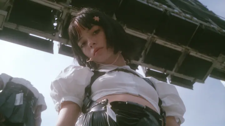 low-angle medium shot of a young Caucasian American woman with pale skin and light freckles, a glossy black blunt jaw-length bob with heavy bangs and one clay-orange streak through the bangs, a small flat clay-orange…