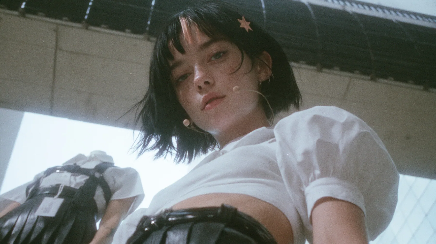 low-angle medium shot of a young Caucasian American woman with pale skin and light freckles, a glossy black blunt jaw-length bob with heavy bangs and one clay-orange streak through the bangs, a small flat clay-orange…