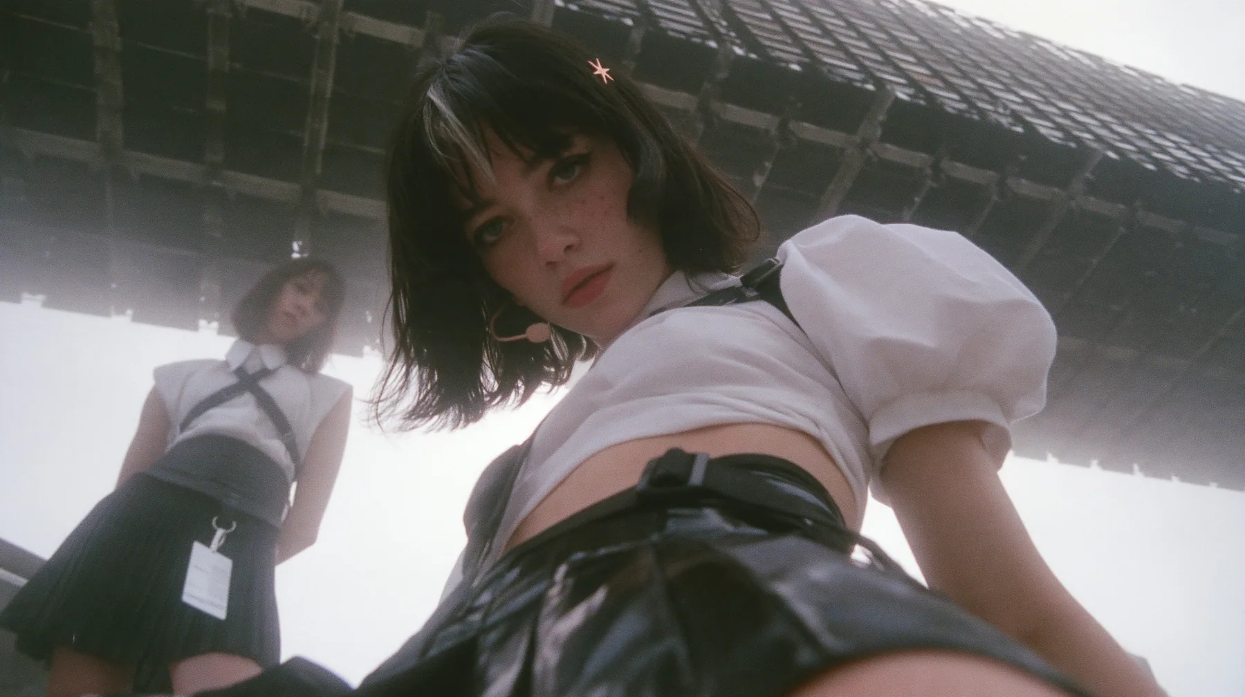 low-angle medium shot of a young Caucasian American woman with pale skin and light freckles, a glossy black blunt jaw-length bob with heavy bangs and one clay-orange streak through the bangs, a small flat clay-orange…