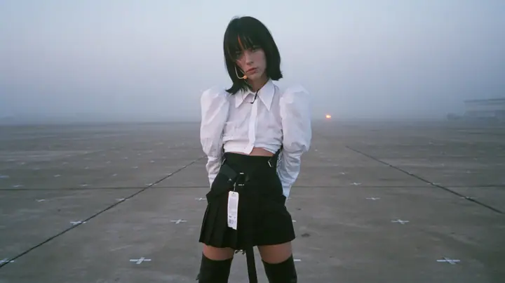 extreme wide shot of a vast empty grey concrete hall with a perfect grid of small painted floor marks receding to the horizon, a young Caucasian American woman with pale skin and light freckles, a glossy black blunt…