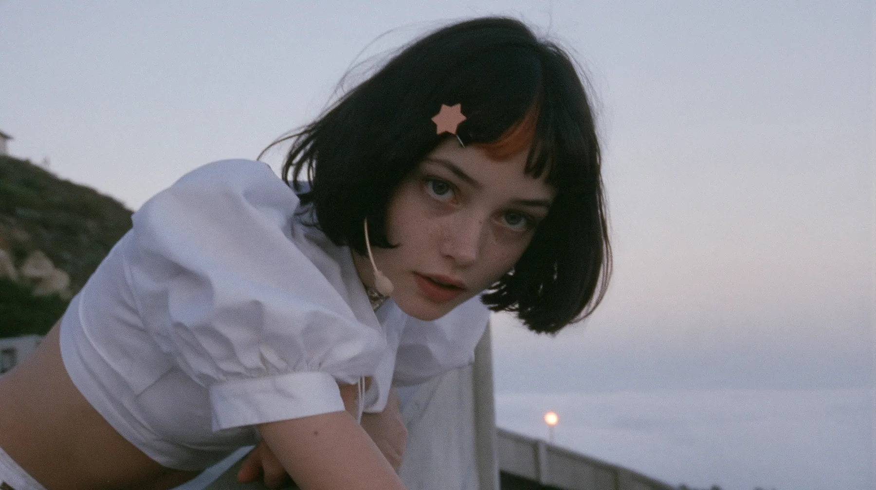 medium close-up of a young Caucasian American woman with pale skin and light freckles, a glossy black blunt jaw-length bob with heavy bangs and one clay-orange streak through the bangs, a small flat clay-orange…