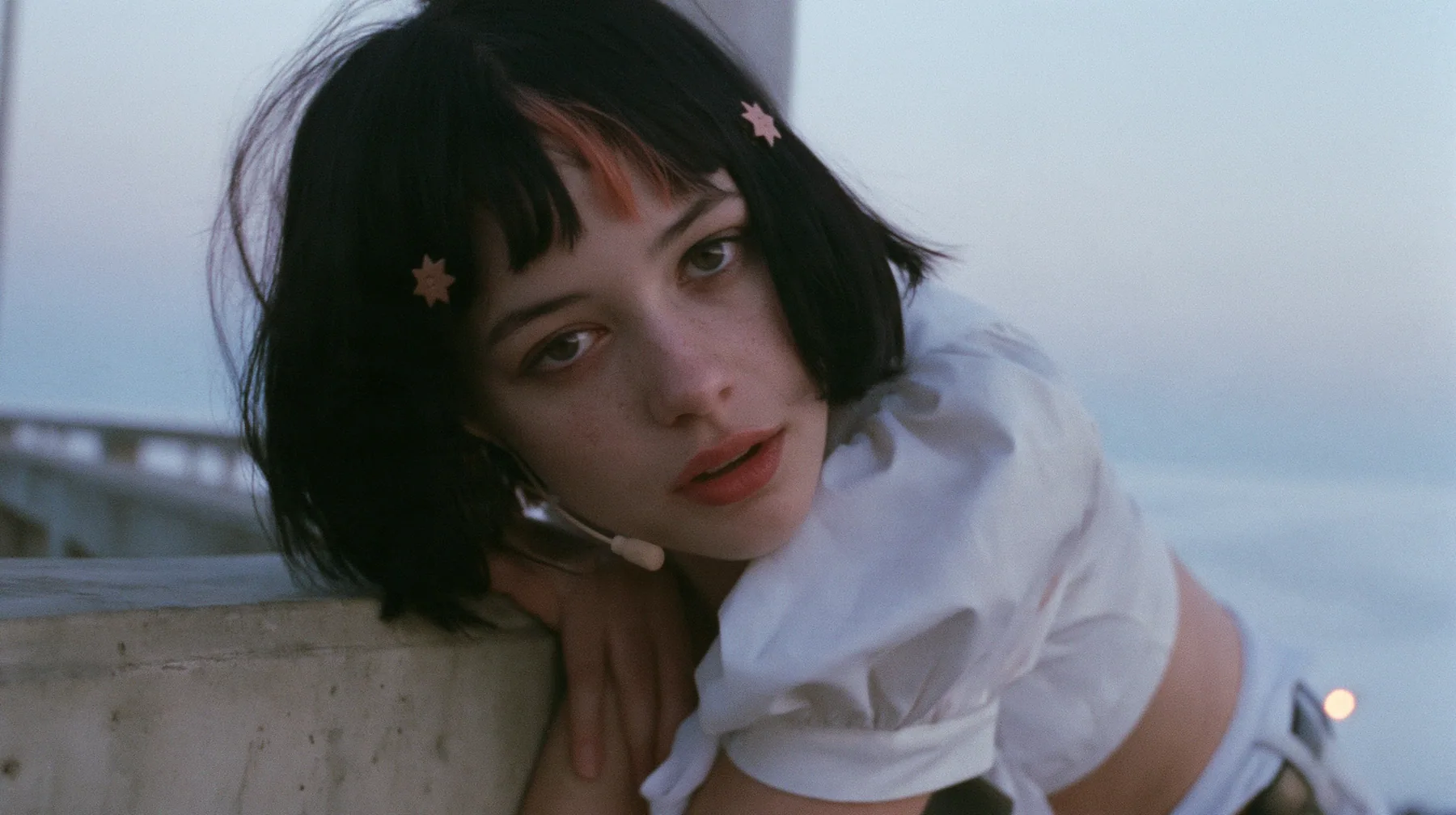 medium close-up of a young Caucasian American woman with pale skin and light freckles, a glossy black blunt jaw-length bob with heavy bangs and one clay-orange streak through the bangs, a small flat clay-orange…
