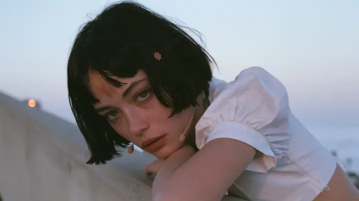 medium close-up of a young Caucasian American woman with pale skin and light freckles, a glossy black blunt jaw-length bob with heavy bangs and one clay-orange streak through the bangs, a small flat clay-orange…