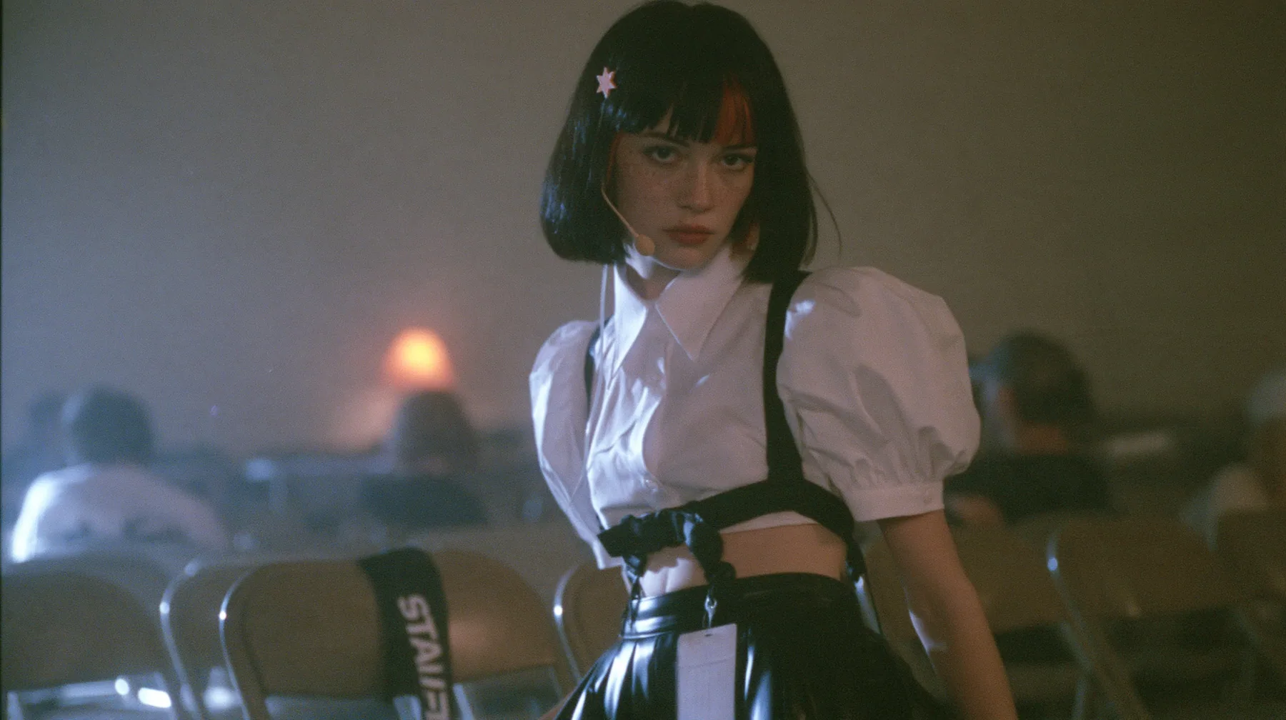 medium shot of a young Caucasian American woman with pale skin and light freckles, a glossy black blunt jaw-length bob with heavy bangs and one clay-orange streak through the bangs, a small flat clay-orange…