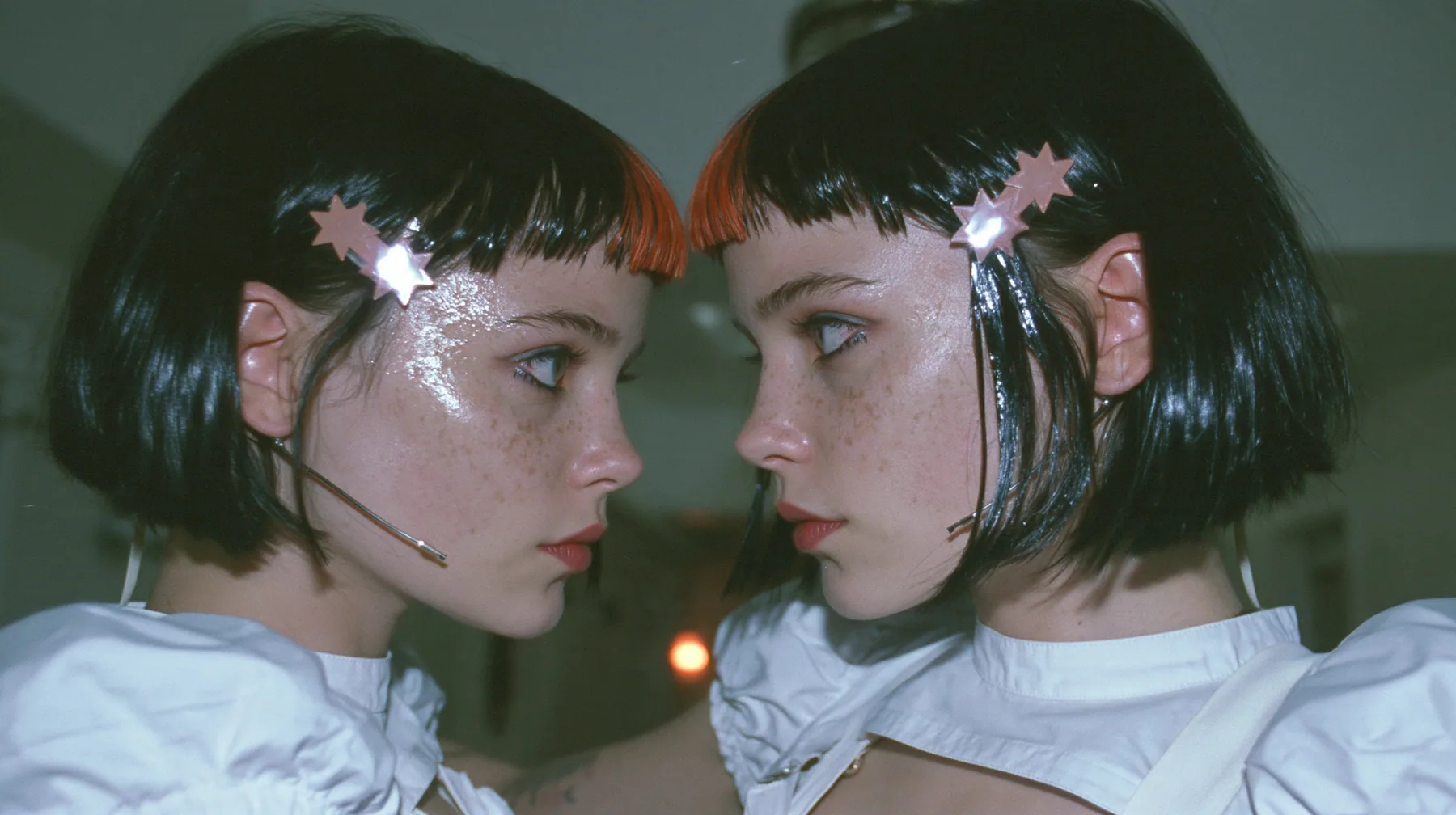 medium close-up of two identical copies of a young Caucasian American woman with pale skin and light freckles, a glossy black blunt jaw-length bob with heavy bangs and one clay-orange streak through the bangs, a…